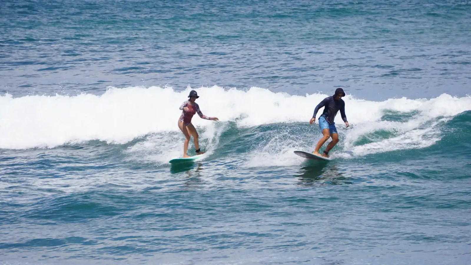 Two beginner surfers riding a small, clean wave at Beginners Bay, Popoyo, Nicaragua