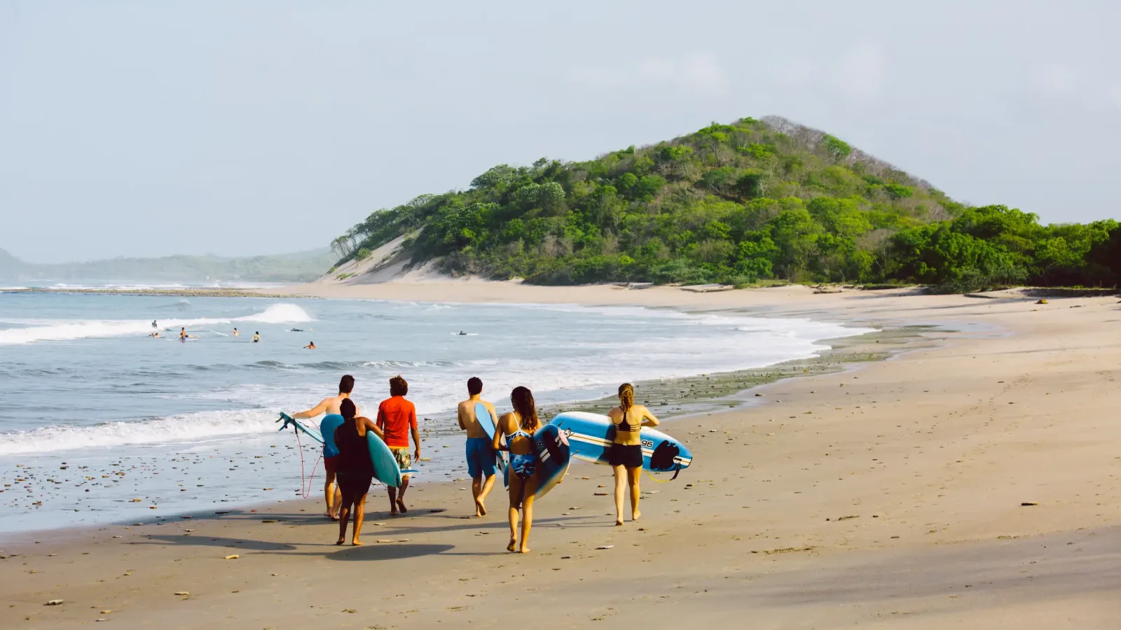 Group of surfers carrying boards along the beach towards the waves at Popoyo, Nicaragua